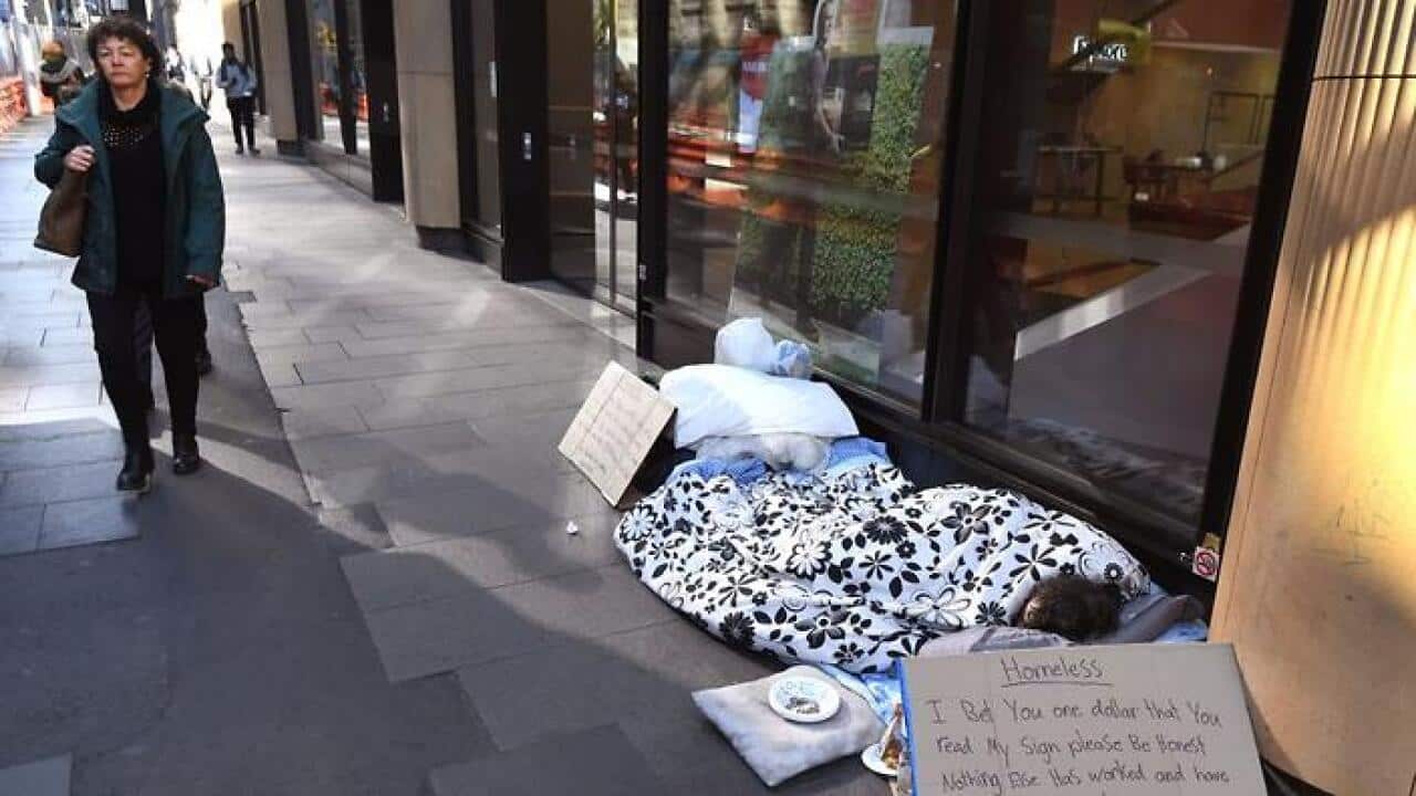 A homeless man (R) lies on the ground in front of a store begging for money in Sydney's central business district (CBD) on July 10, 2017. / AFP PHOTO / William WEST (Photo credit should read WILLIAM WEST/AFP/Getty Images)