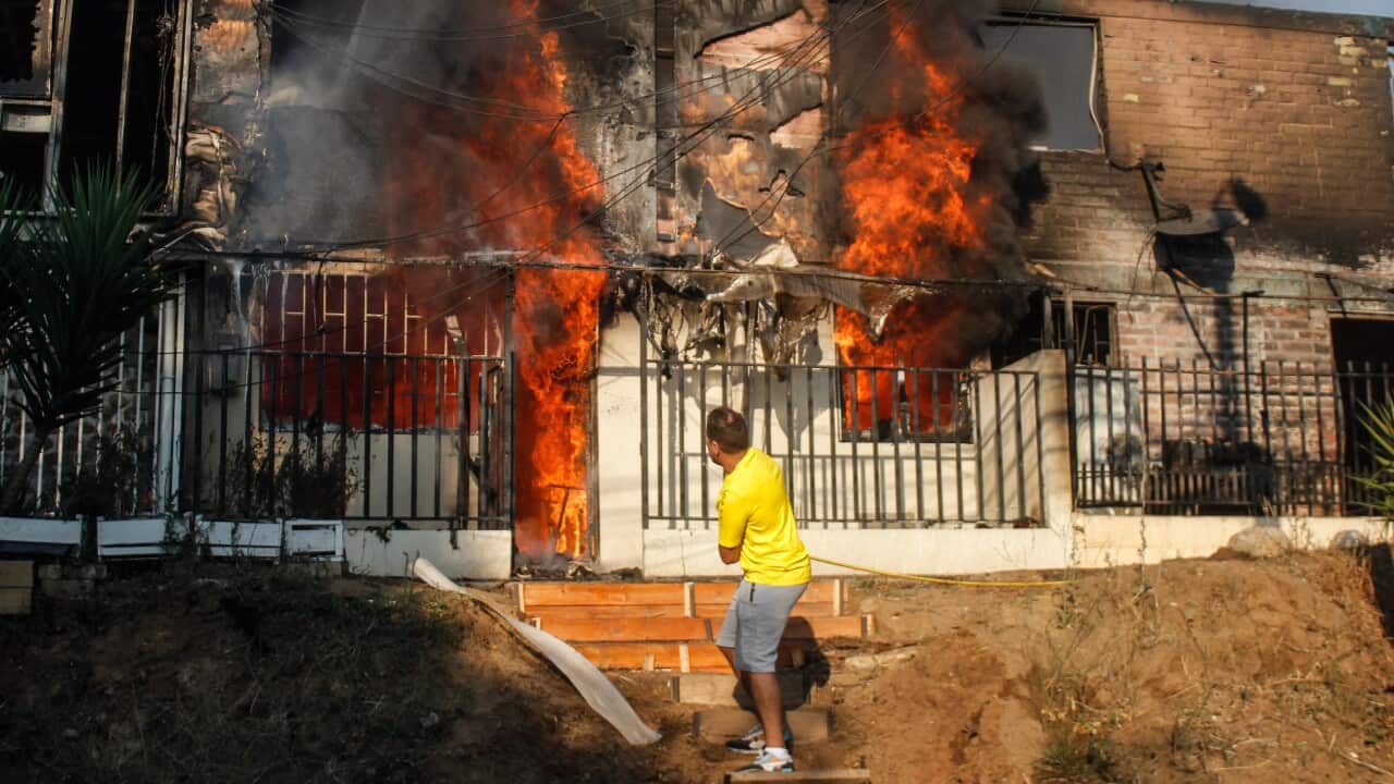 A man tries to put out the flames of a burning house with a hose.