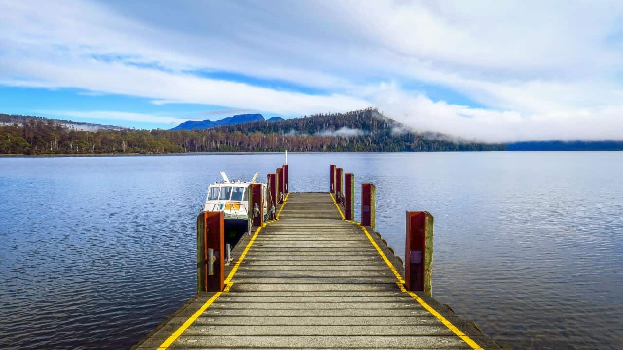 A small jetty extends into a lake, with a boat tied up on its side. In the distance, low clouds engulf wooded hills.