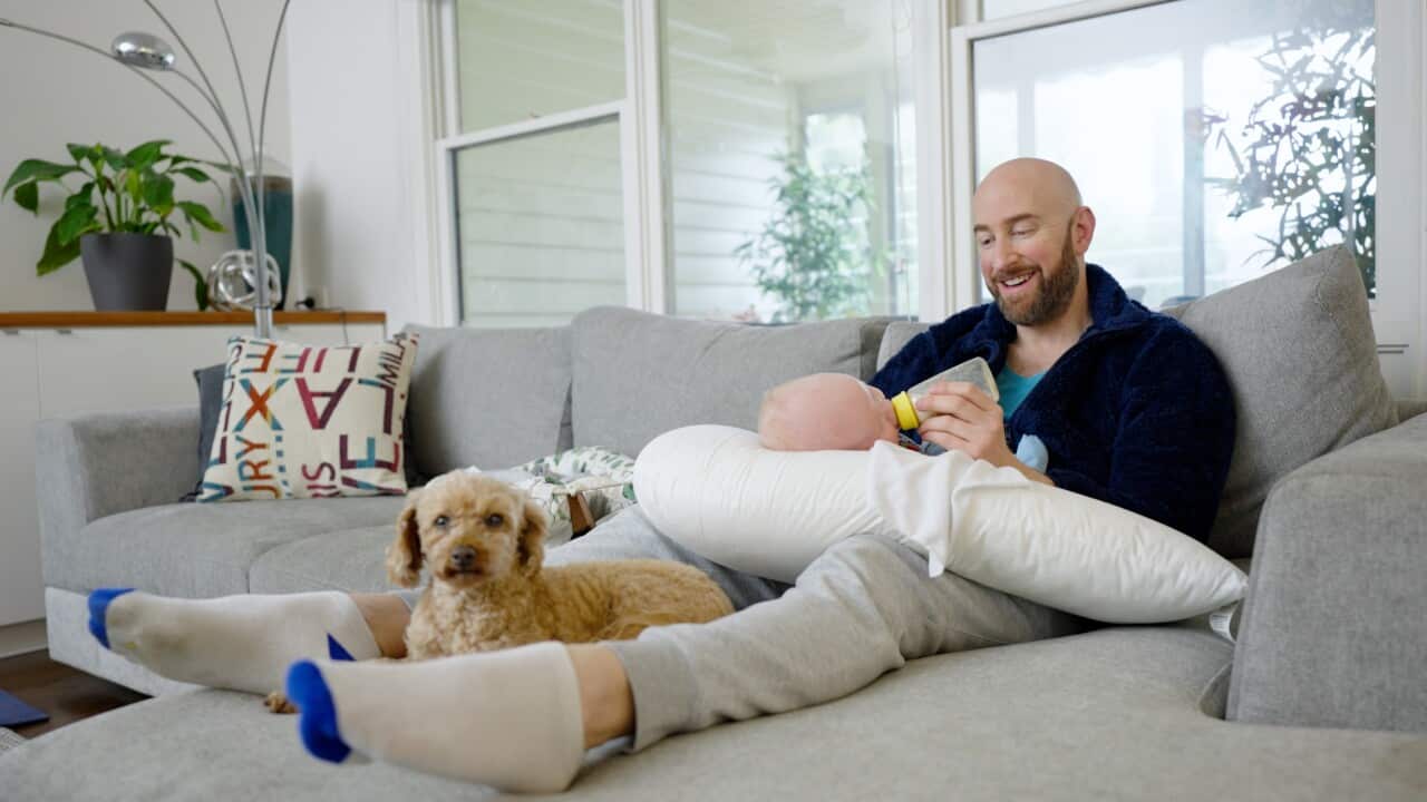 Shaun Resnik feeding his baby Eli on the couch in their Melbourne home