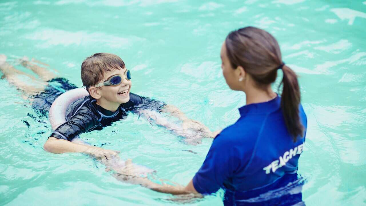 Young boy learning to swim in pool with teacher
