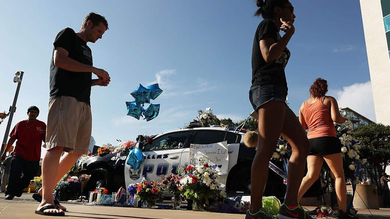 People write condolence notes and lay flowers at a growing memorial in front of the Dallas Police Headquarters near the area that is still an active