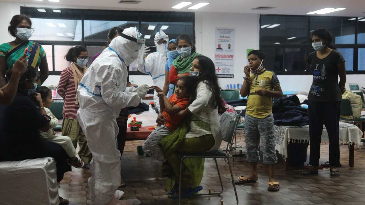 A healthcare worker wearing a PPE suit offers sweets to a child of a Covid-19 patient wearing a mask at the COVID-19 isolation centre.