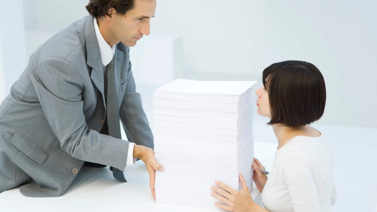 Boss pushing stack of paper across desk to his assistant