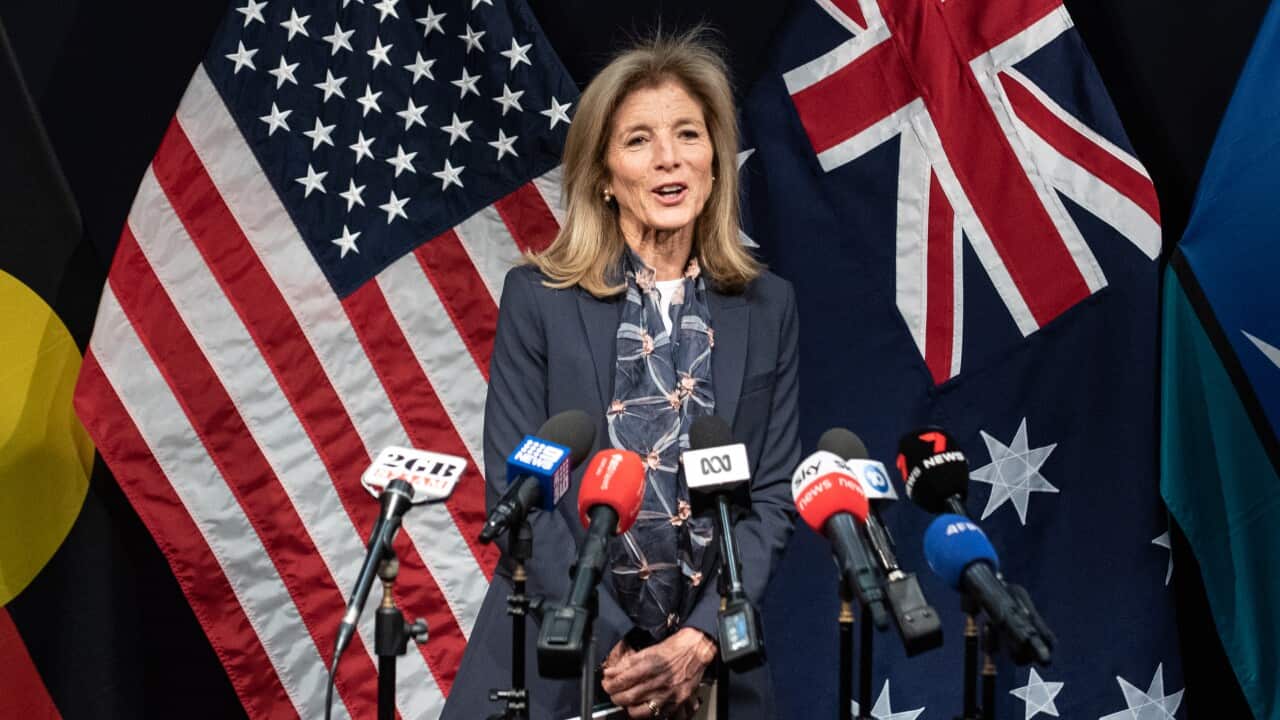 Caroline Kennedy stands in front of four flags, speaking.