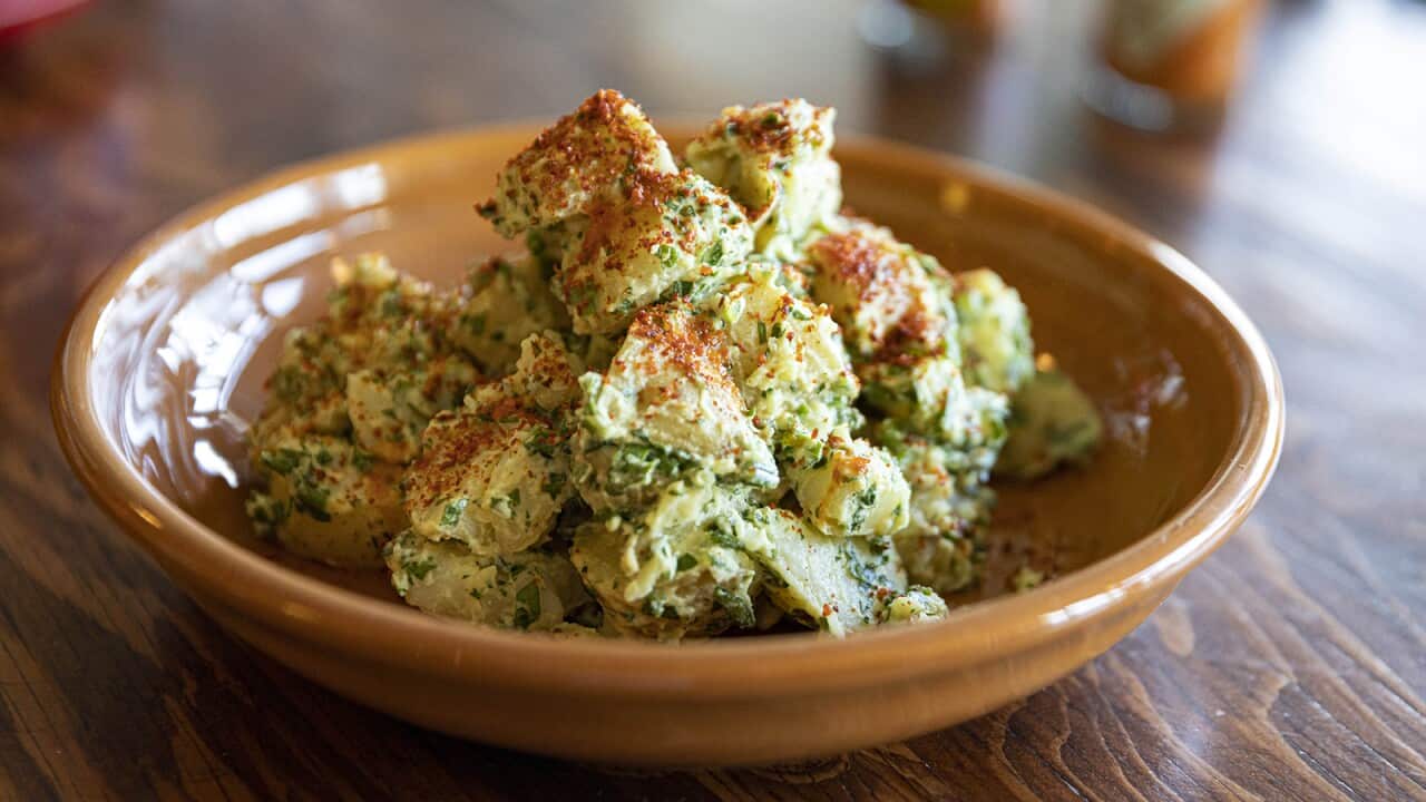 A chunky potato salad with green-flecked dressing sits in a brown pottery serving dish.