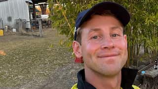 A man smiling in a hi-vis shirt and a hat.