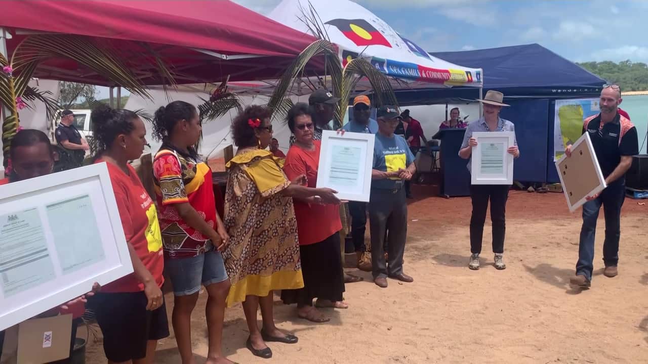 QLD premier hands certificates to traditional owners standing amongst the sand