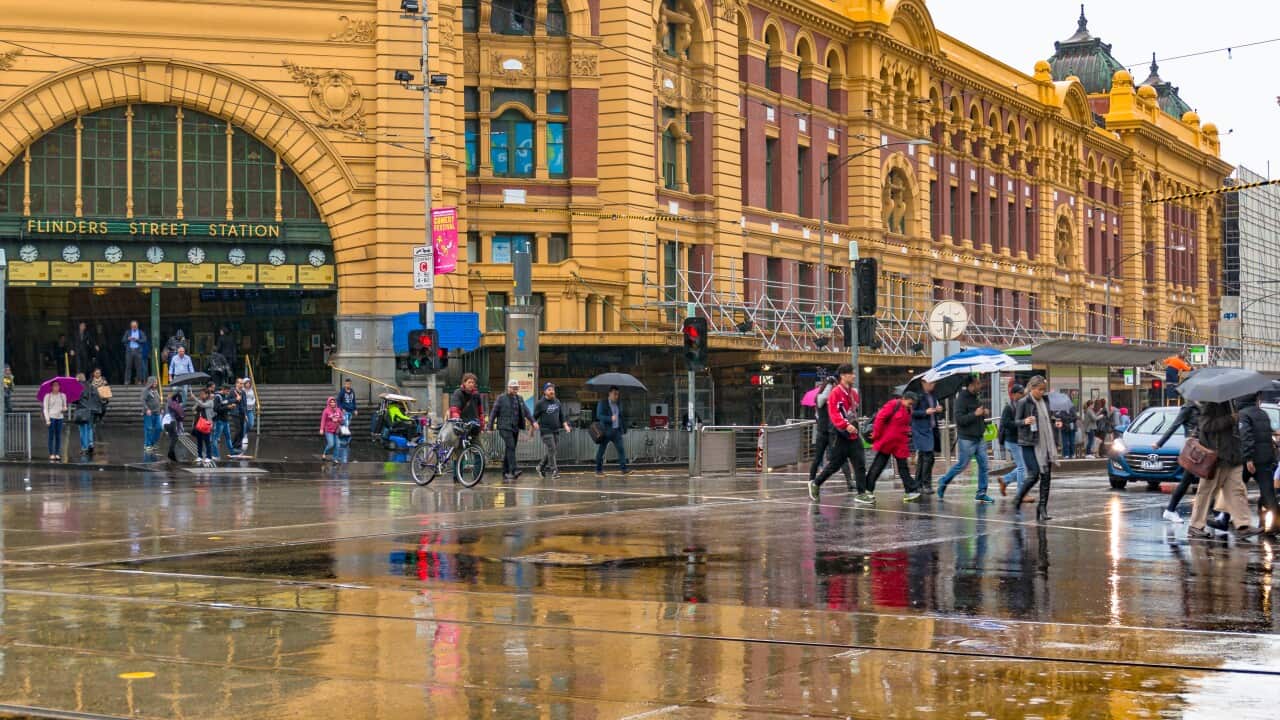 Pedestrians crossing road in front of Flinders street station on rainy day