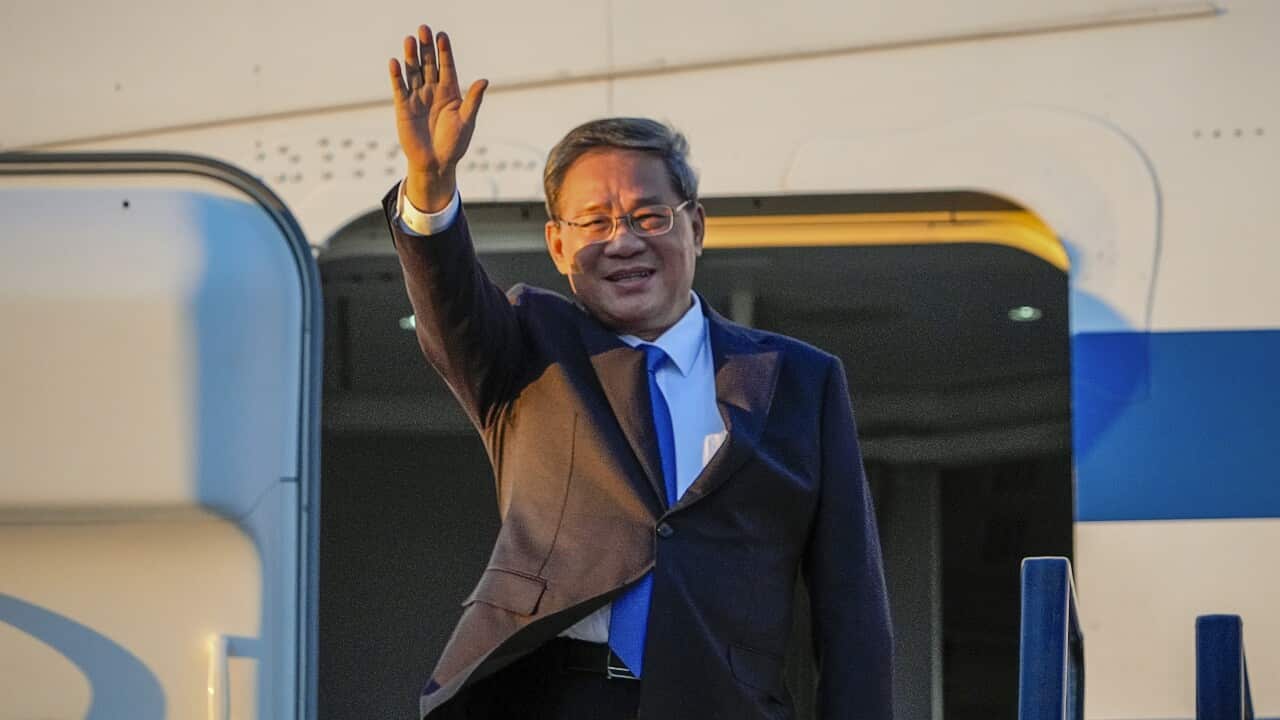 Man in a suit waves as he steps out of a plane.