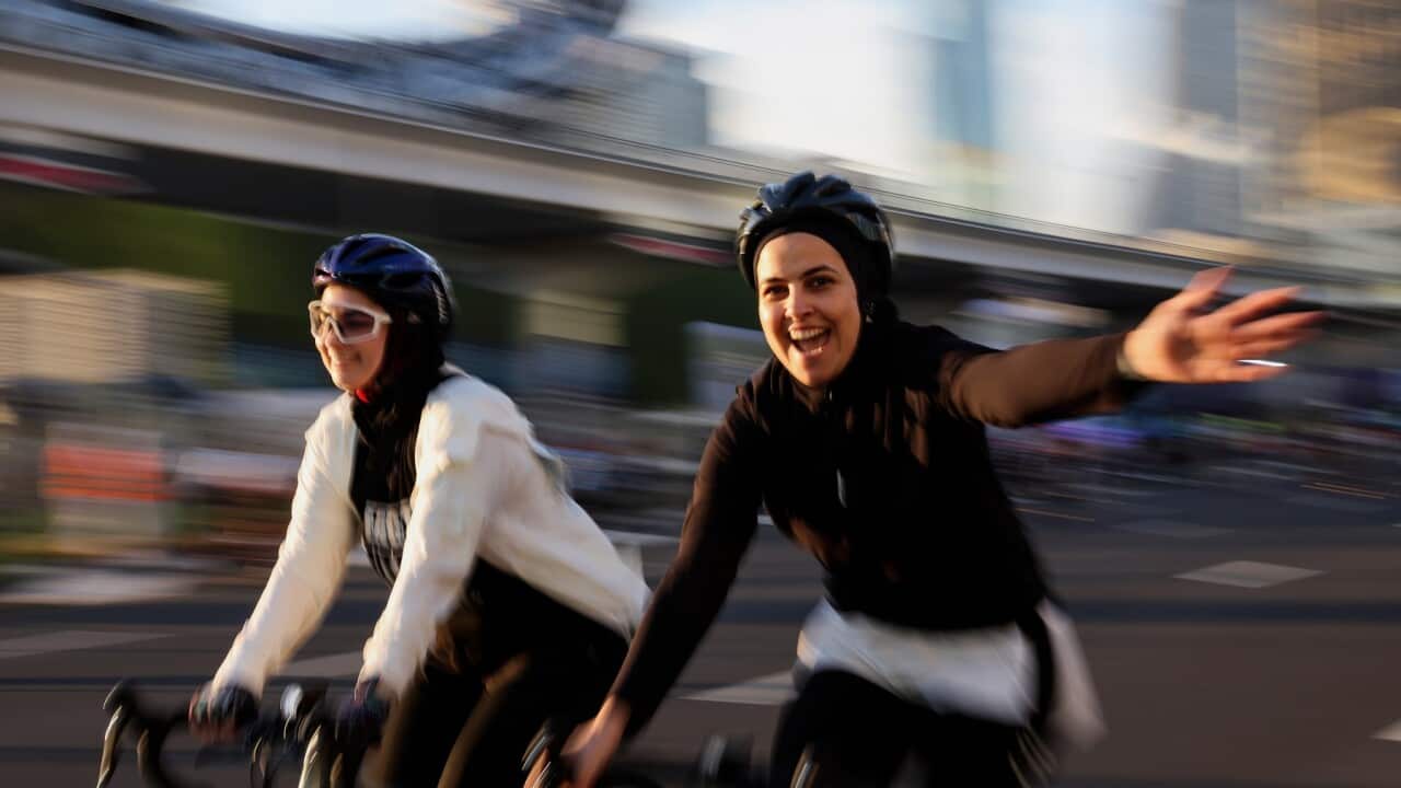 Female cyclists smile and wave.