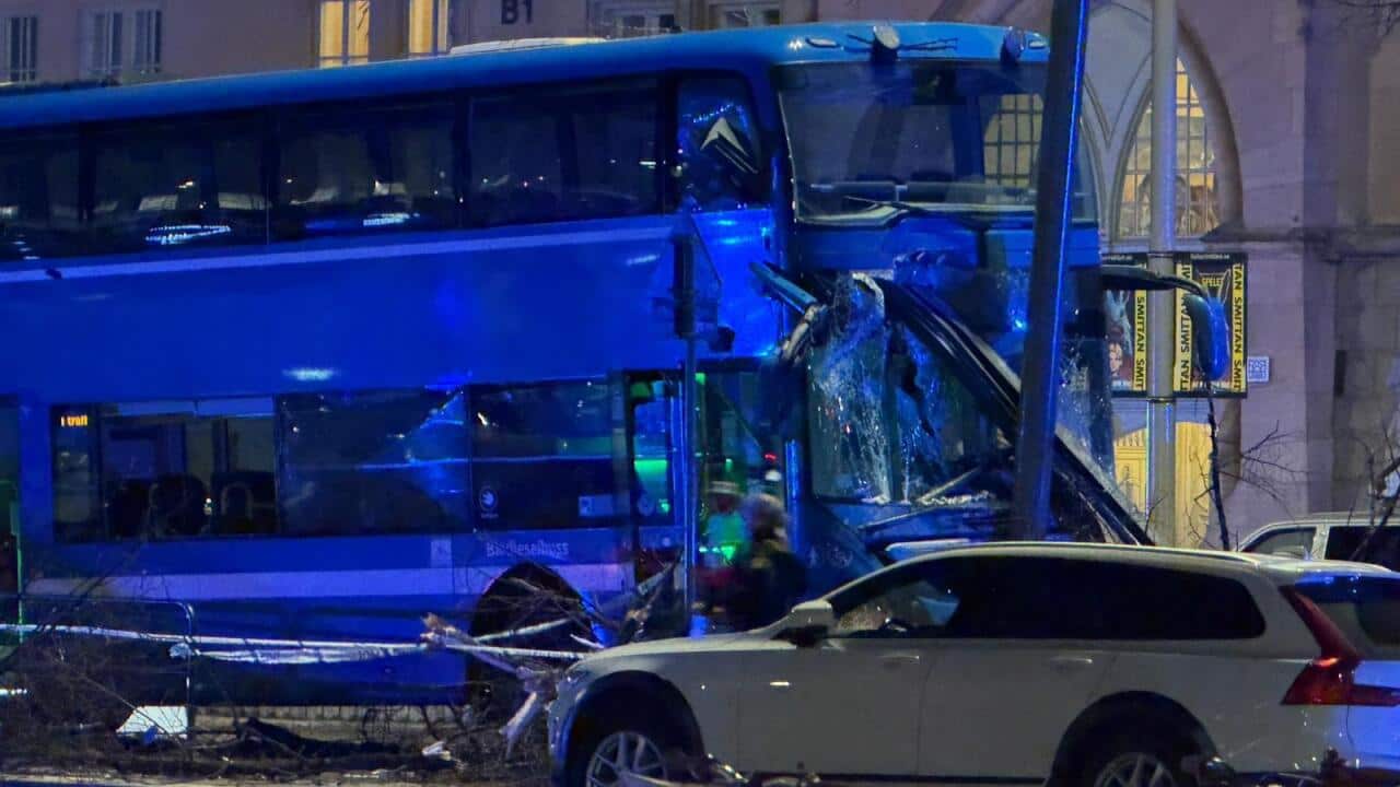 A double decker bus with its front smashed into a pole. Police tape surrounds the scene.