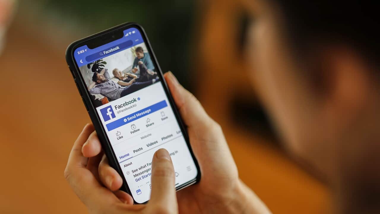 A person holds a smartphone displaying the Facebook app.