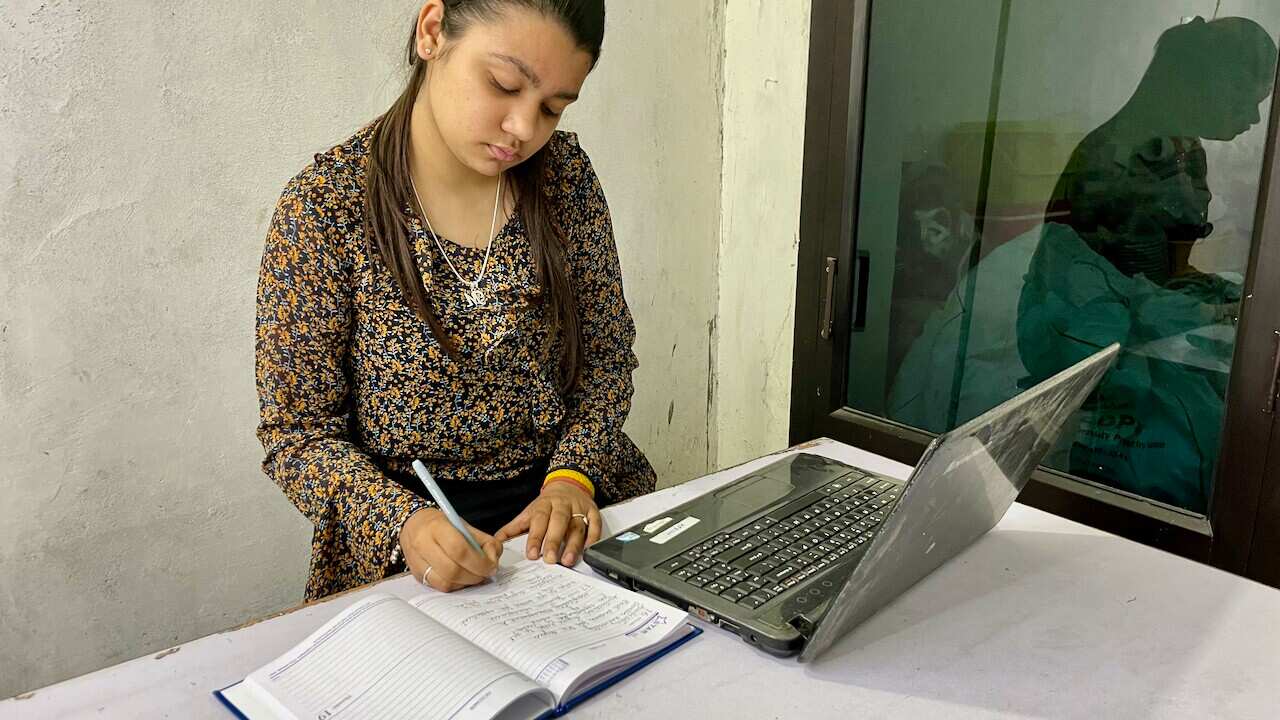 A woman writes in a notebook next to an open laptop