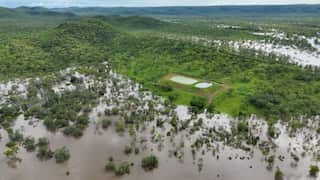 An aerial photo taken near the Northern Territory township of Daly River. Brown floodwater covers most of the lower landscape, while hilly higher ground in the background remains lush and green.