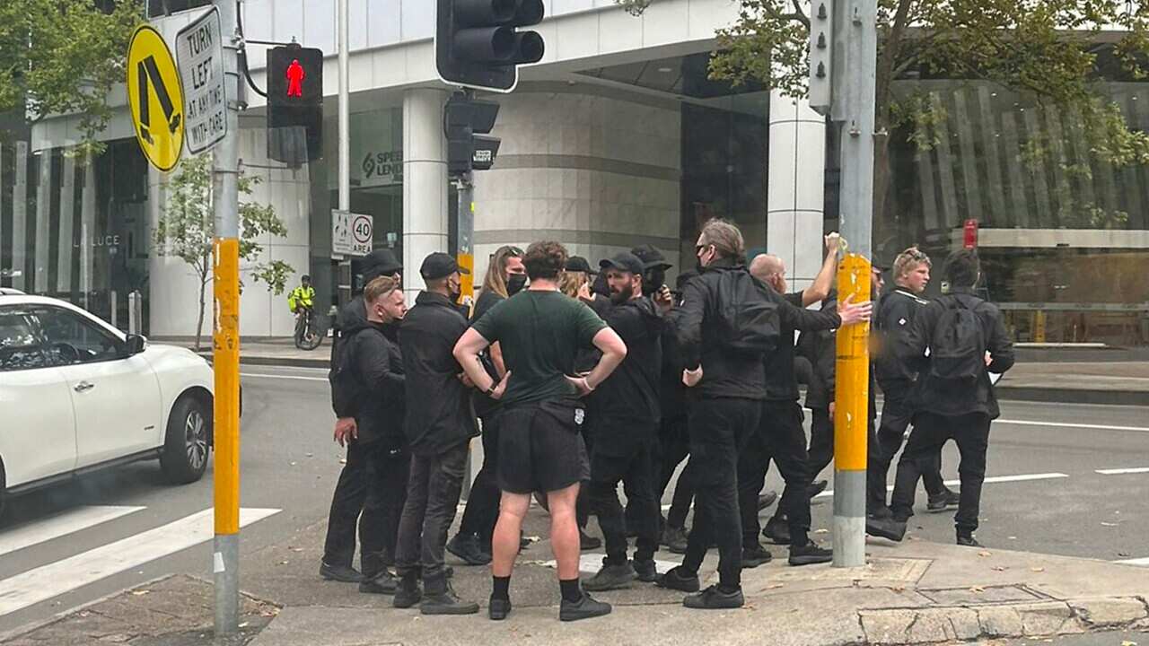 A group of men wearing black cross the road near North Sydney train station.
