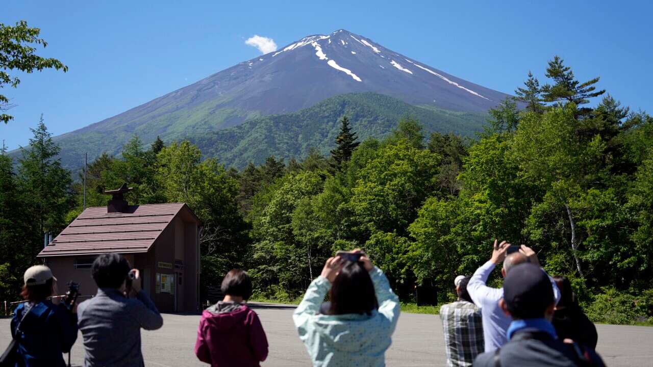 Tourists take a photo of a snow-capped mountain in the distance.