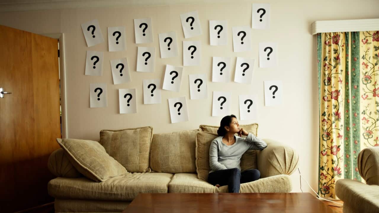 Woman sitting on sofa with question marks on wall.
