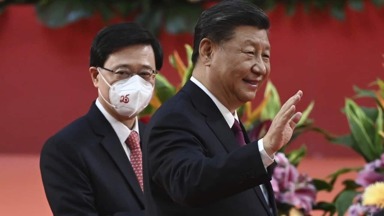 Two men standing. One is smiling and waving, the other is wearing a face mask.