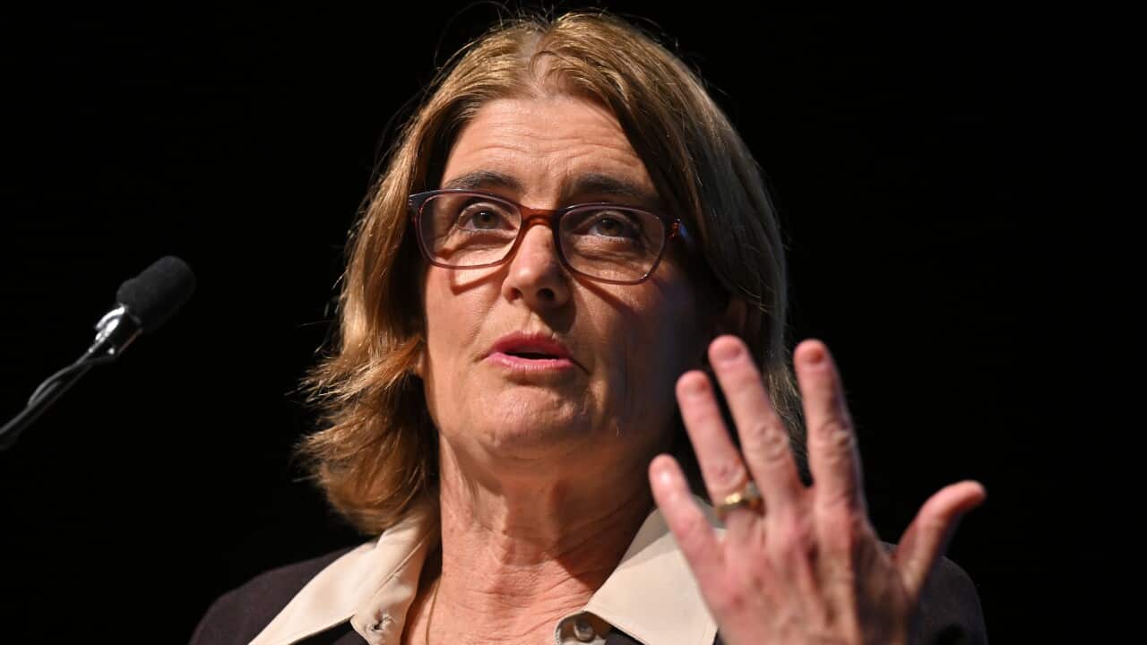 A woman in a suit is talking into a microphone with one hand raised.