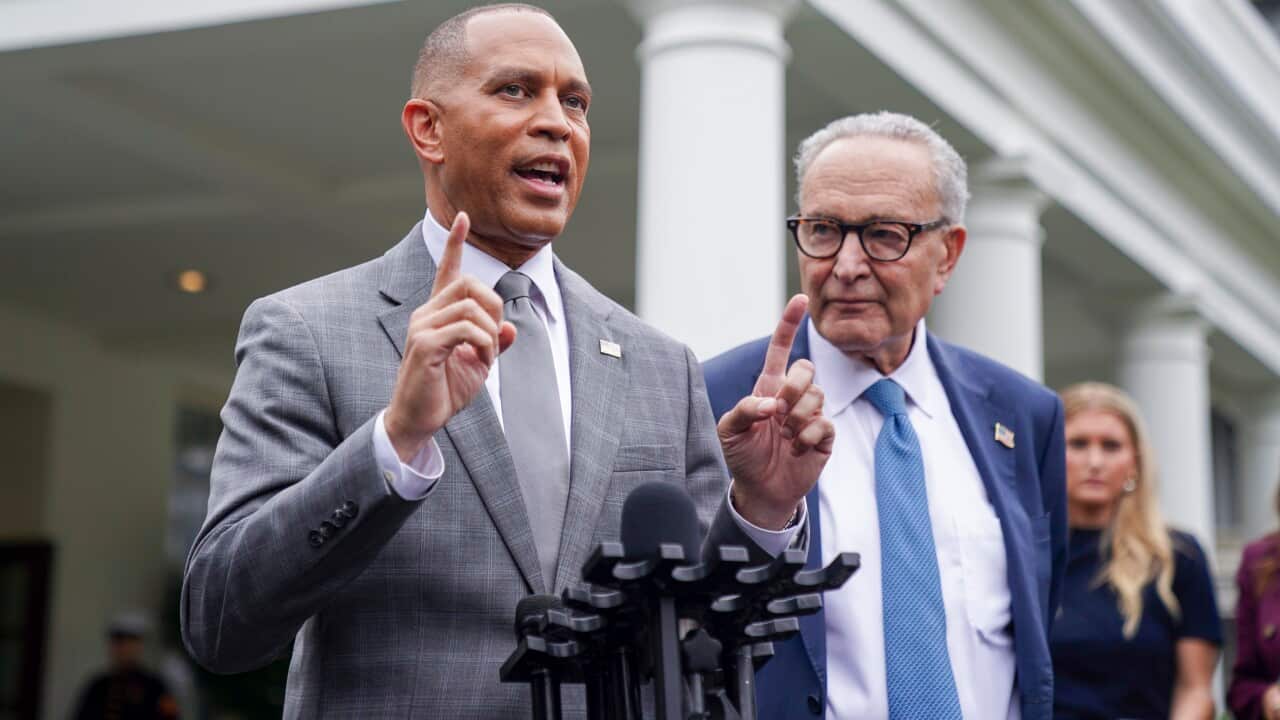 Two people wearing formal attire standing at a microphone. One is speaking.