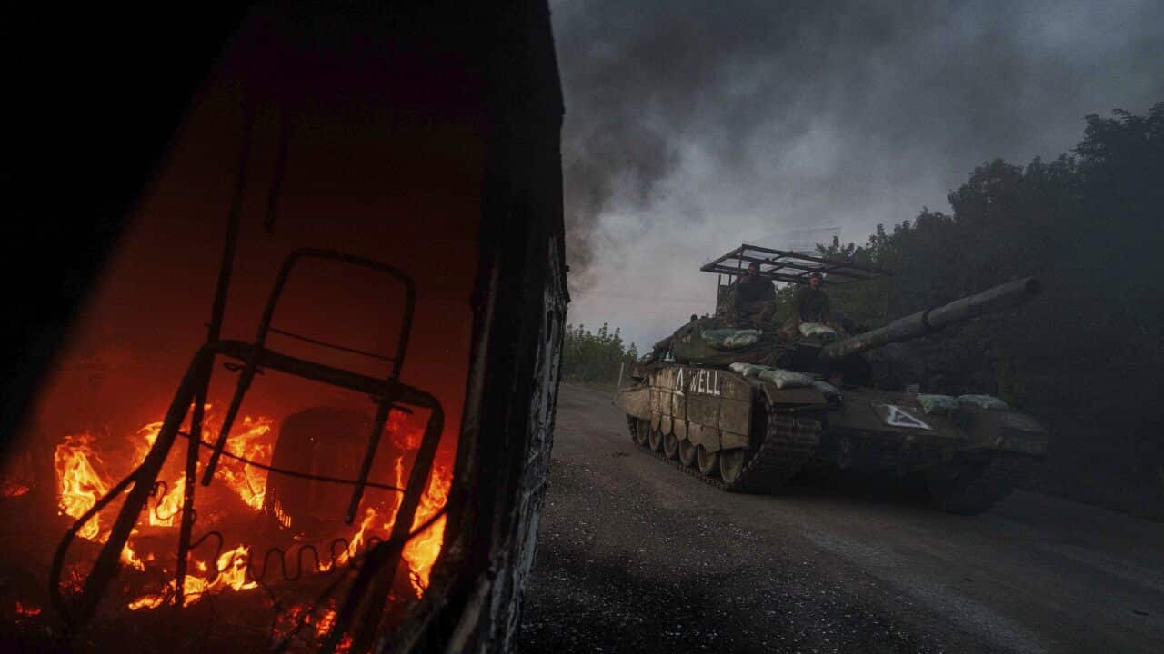 A fire is seen inside a vehicle as it passes a military tank