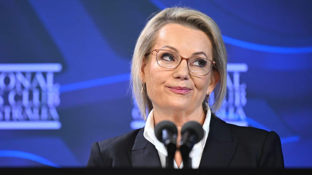 A blonde women in front of a lectern, looking to her left with her lips pursed.