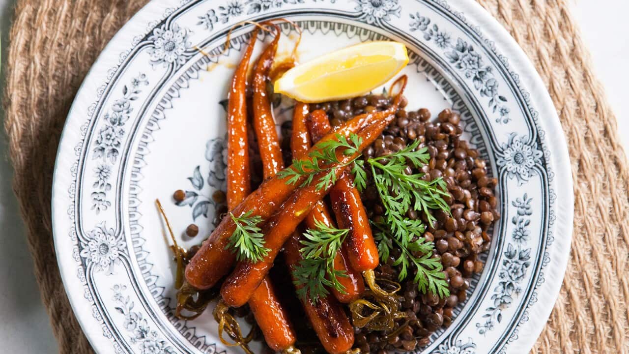 Glazed cooked carrots sit on a mound of lentils on a floral blue and white plate.
