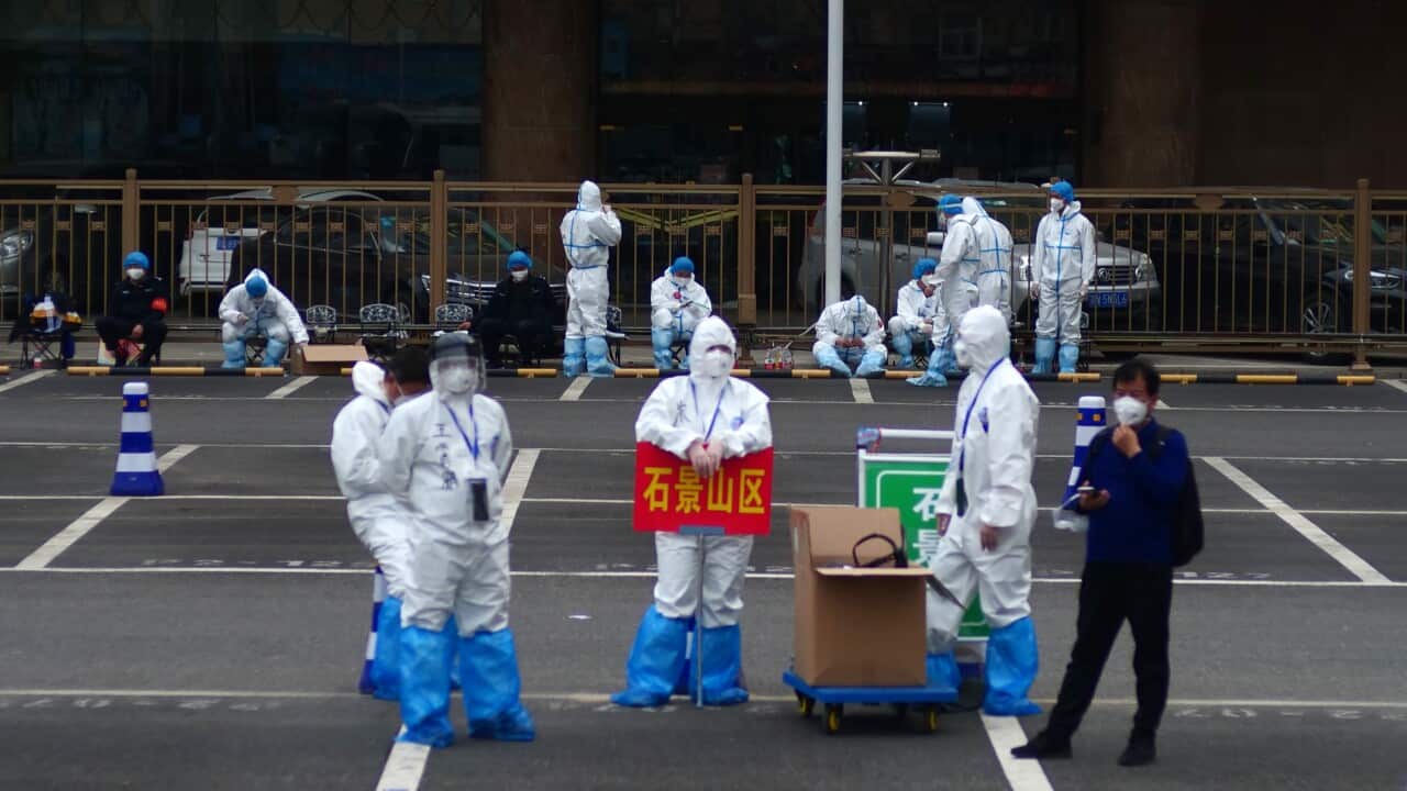workers in full protective gear stand in a parking lot of the West Station in Beijing, China