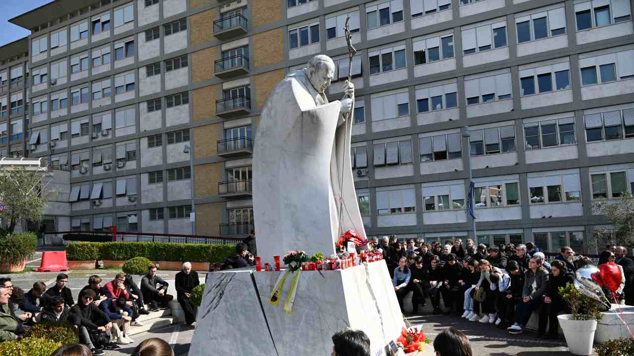 People gather around a statue to pray outside a hospital building.