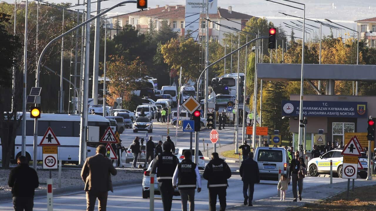 Several people in what could be bullet-proof black vests walk towards a street crowded with haphazardly parked emergency service vehicles.