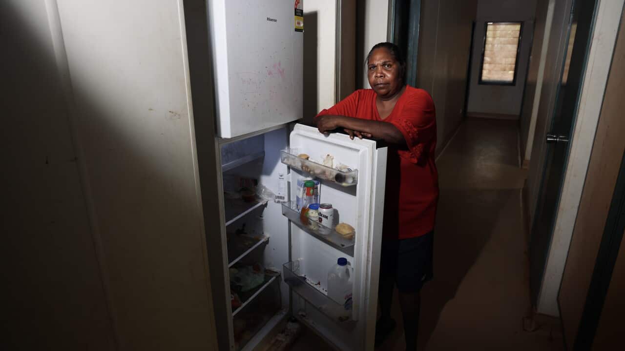 A middle-aged woman in a red top stands over her open fridge.