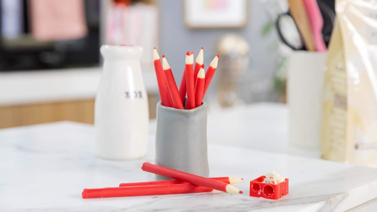 Seven red pencils stand in a tall grey pottery vessel. Three more lie on the table in front.