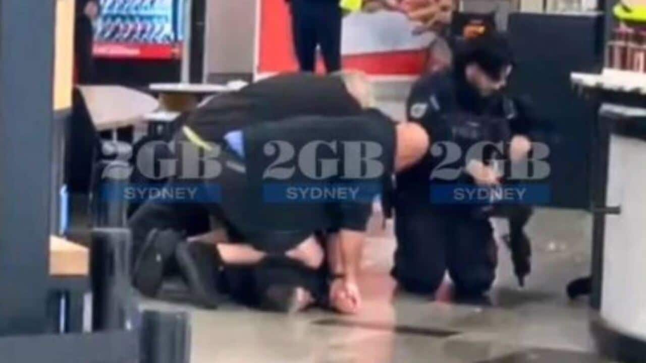 A group of police hold a person down in an airport terminal.