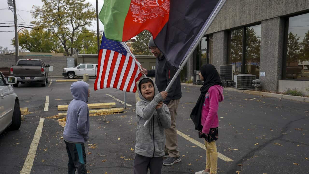 A child waves a flag as two kids and an adult talk in the background