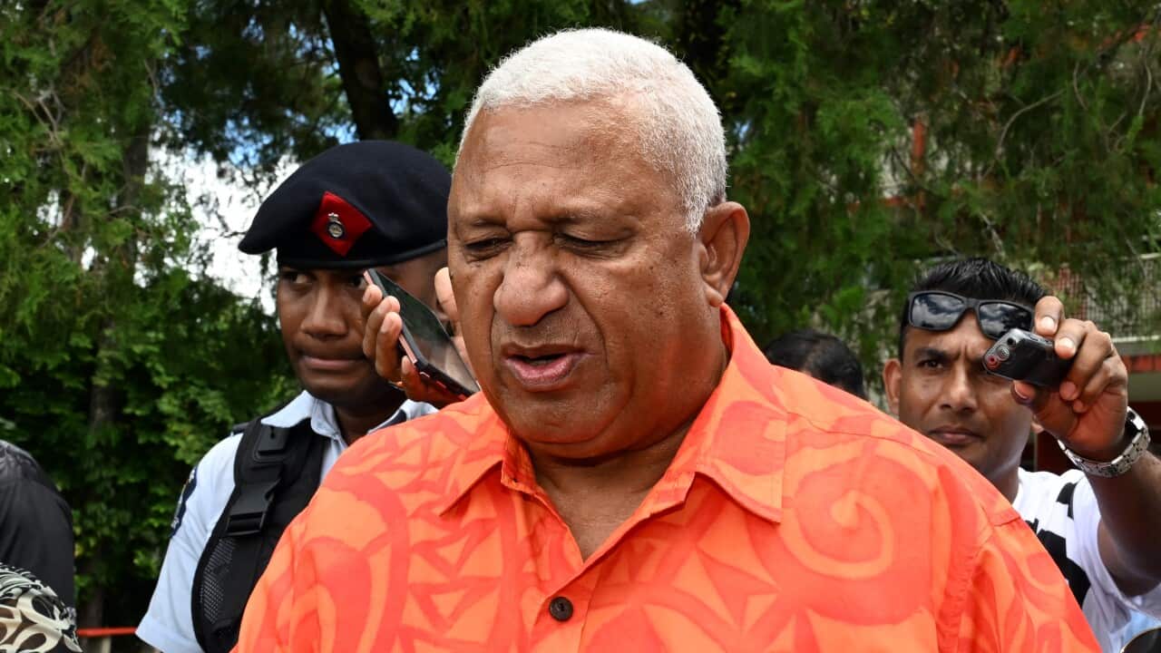 A man in an orange patterned shirt walks outside with people around him.