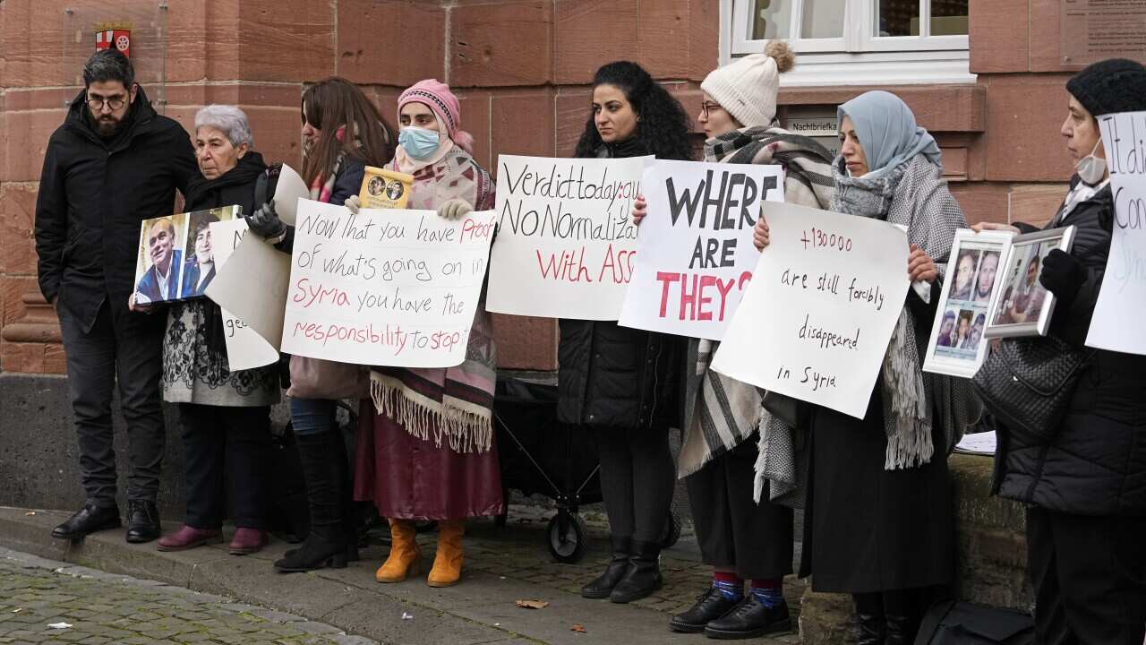 Syrian women holding banners after the verdict in front of the court in Koblenz, Germany, Thursday, Jan. 13, 2022. A German court has convicted a former Syrian secret police officer of crimes against humanity for overseeing the abuse of detainees at a jai