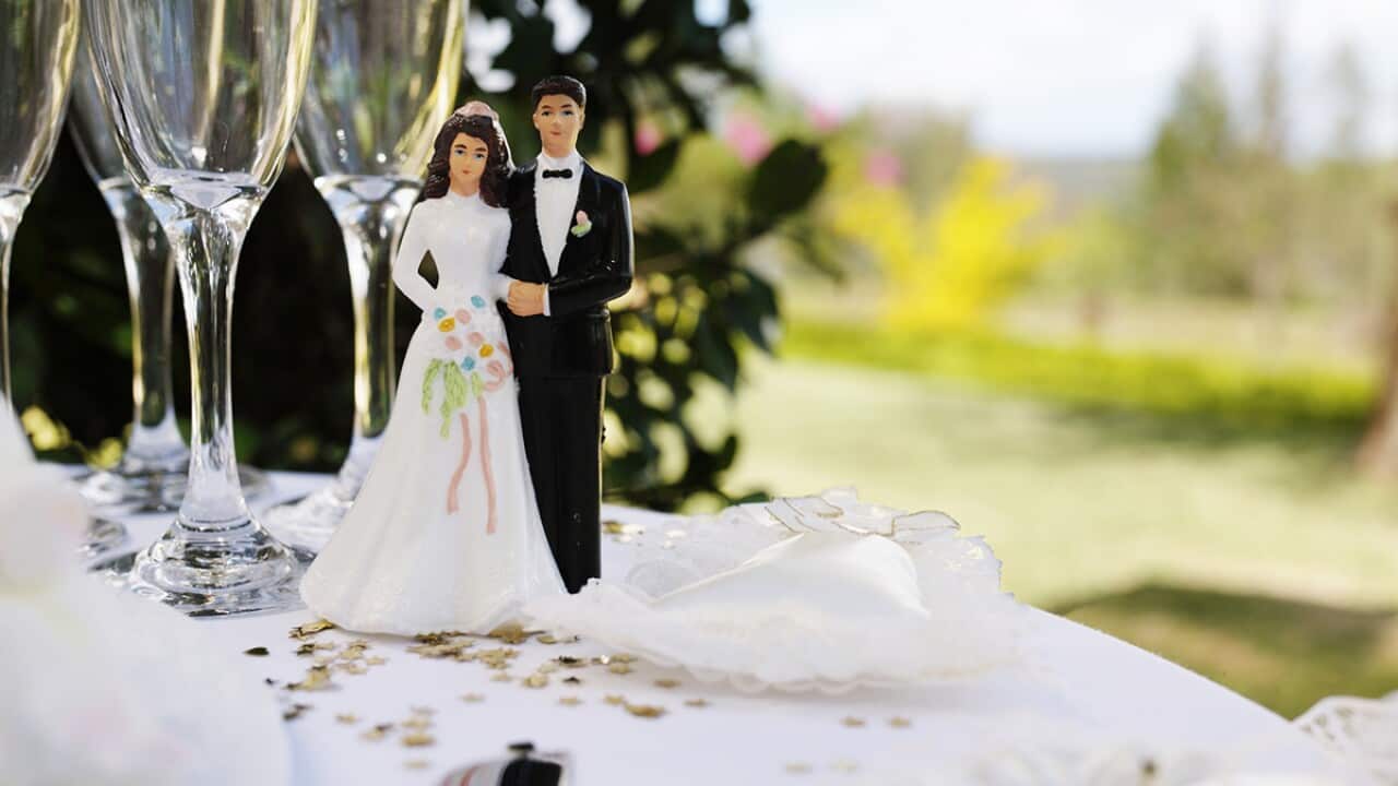 Bride and groom figurine70 per cent of American adults thought that women should take on their husband’s name once they marry. on table by champagne flutes