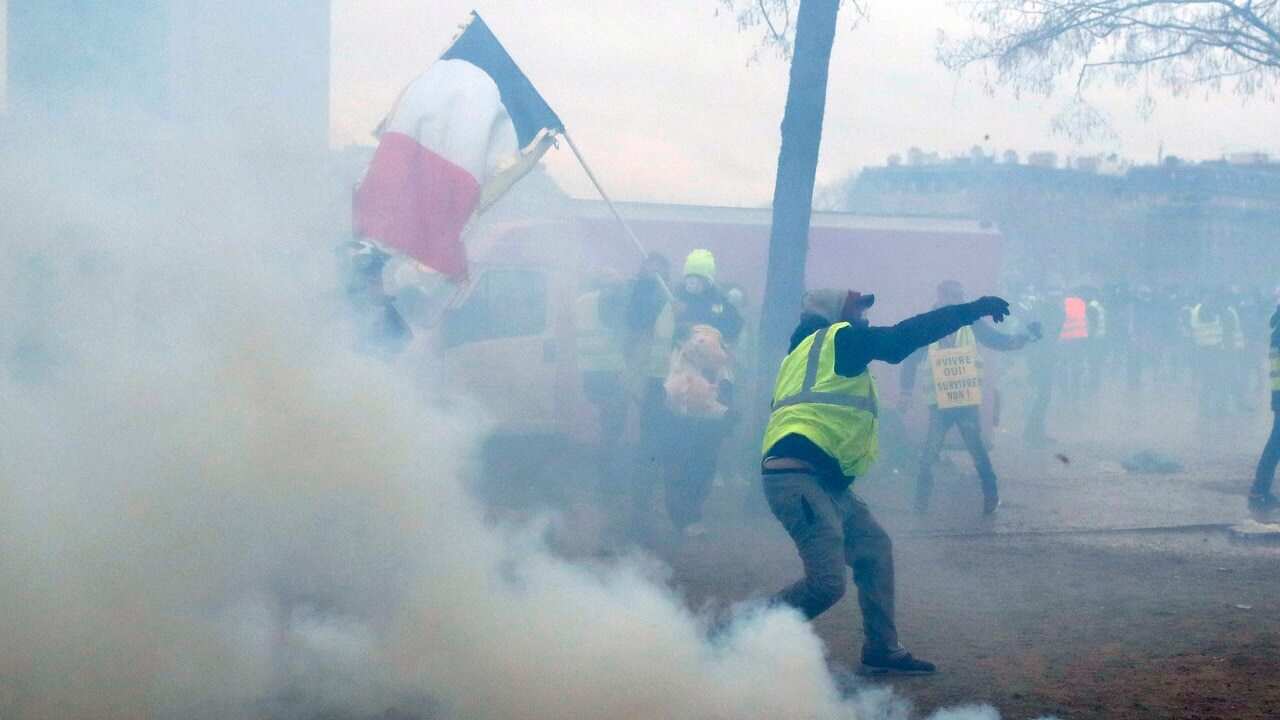 A yellow vest protester throws debris at riot police amid tear gas smoke during clashes around the Arc of Triomphe, in Paris.