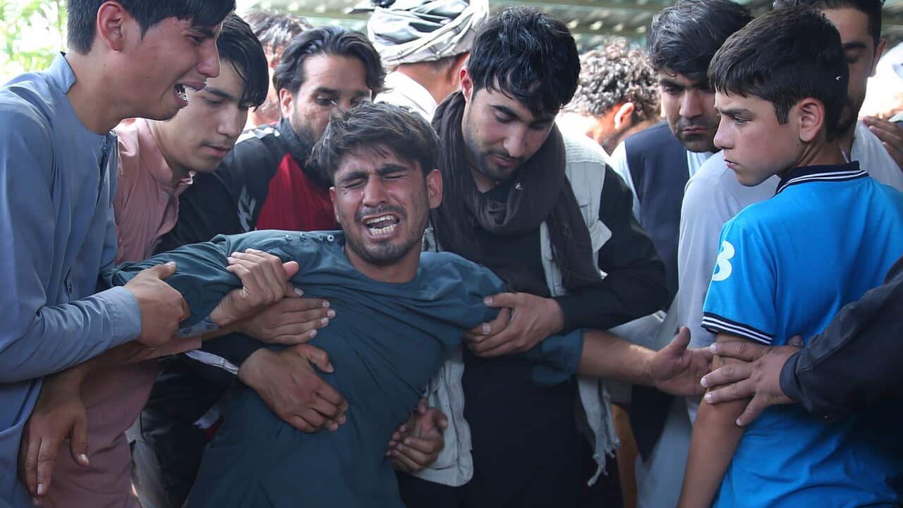 A relative wails near the coffins of victims of the wedding hall bombing in Kabu