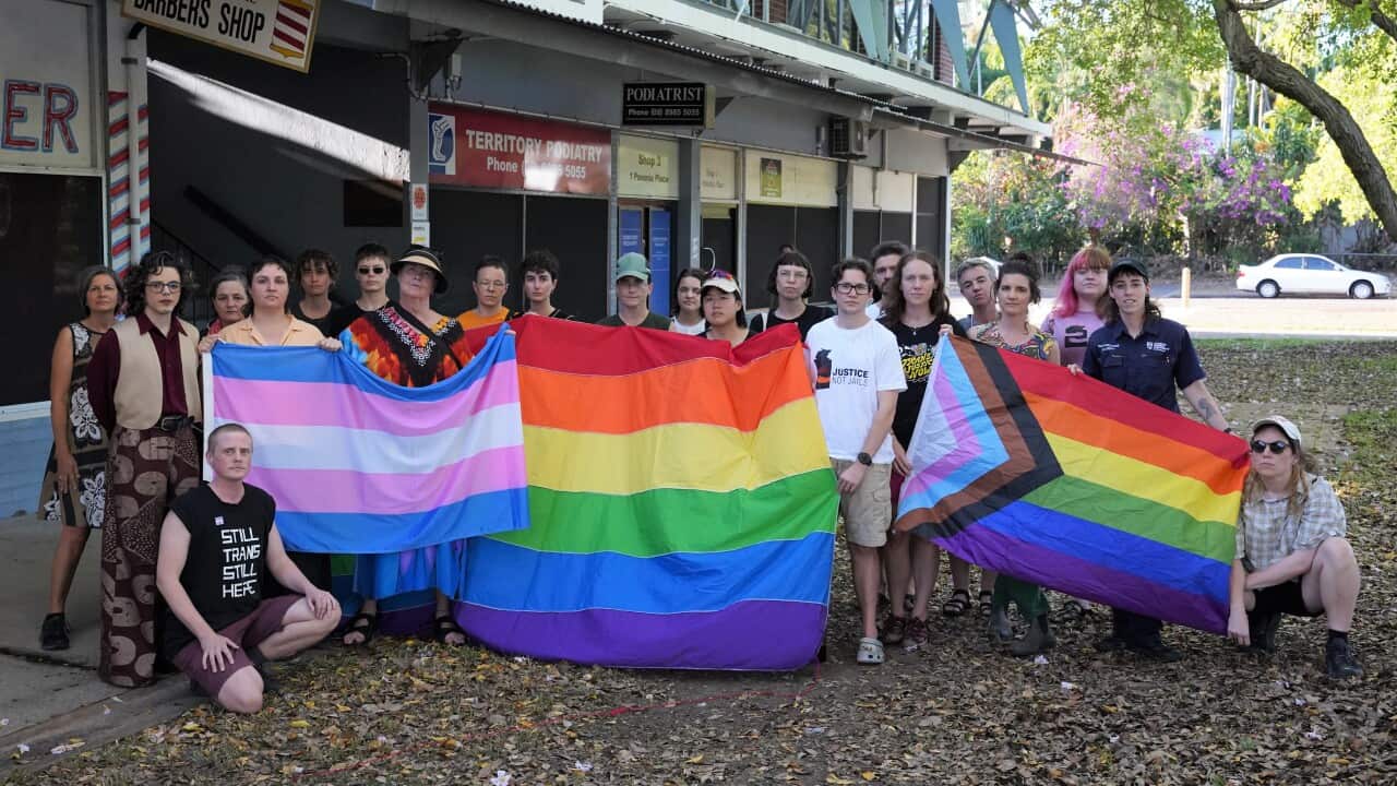 A group of people holding colourful flags that represent parts of the LGBTIQ+ community