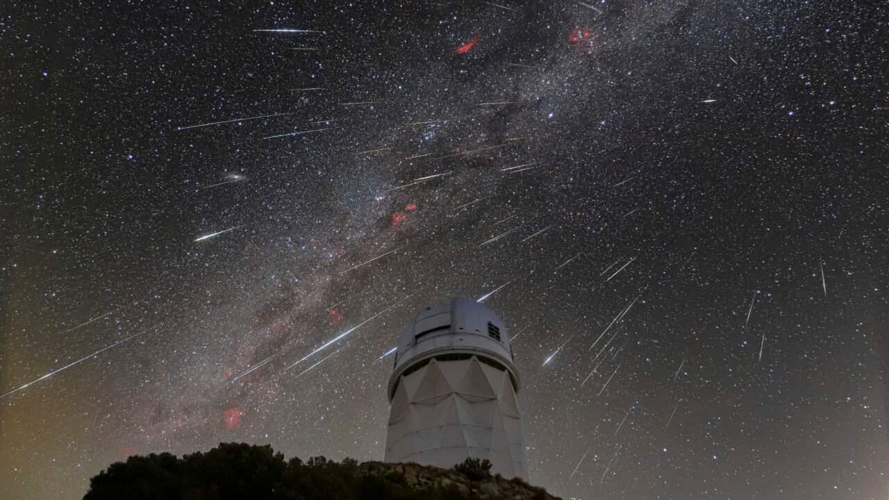 White streaks in night sky above an observatory.