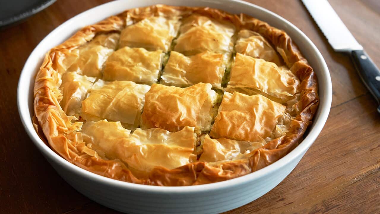 A golden filo pie scored into square pieces sits in a deep, round white pie dish.