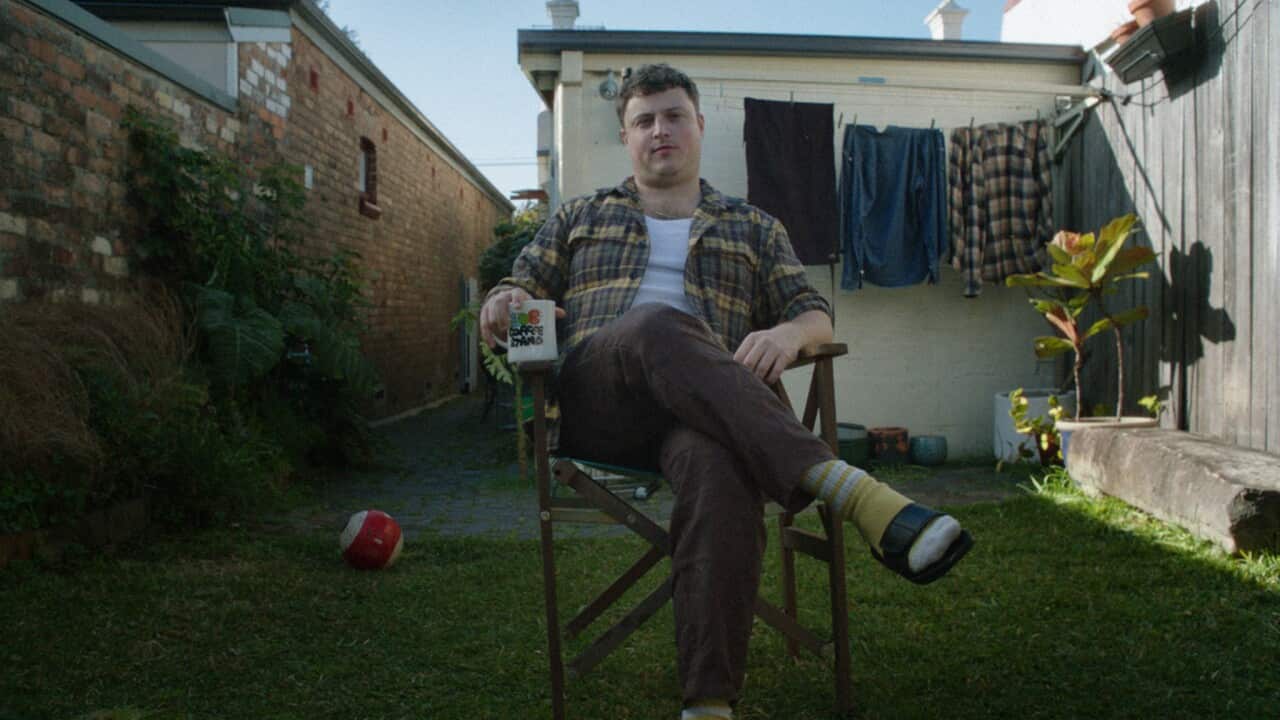 A man sitting cross-legged on a chair in his backyard.