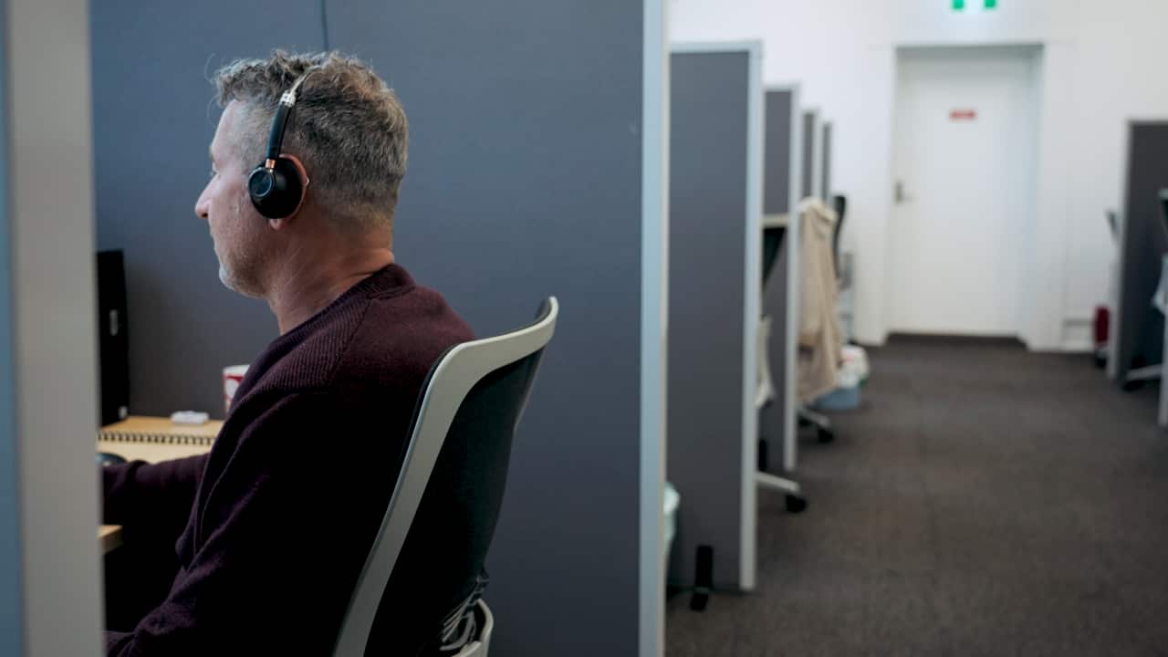 A man sits at his desk with headphones on.