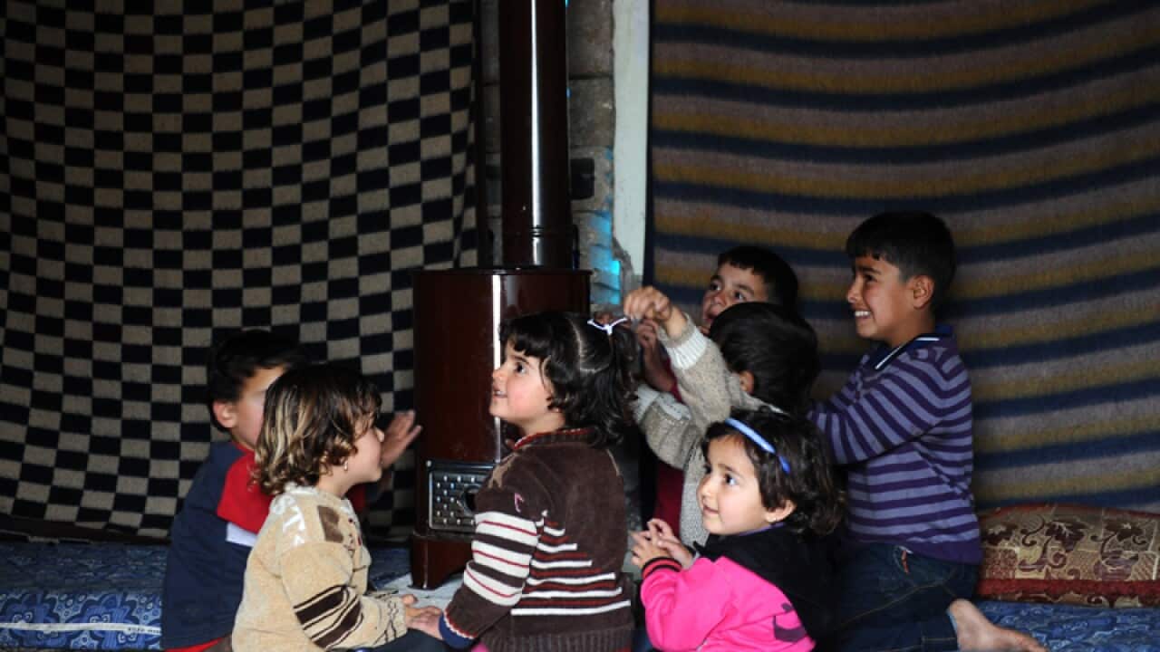 Syrian children gather around a stove in a refugee camp