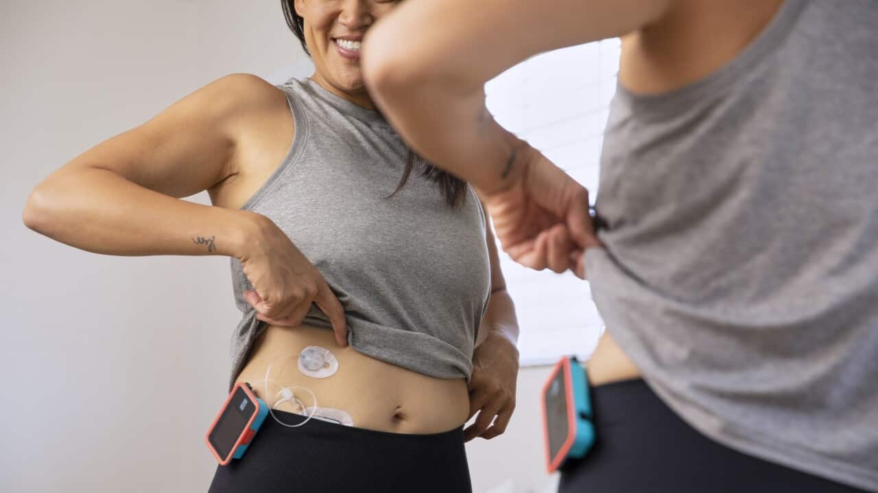 Mirror reflection of woman with type-1 diabetes in workout gear checking her insulin pump and infusion site.