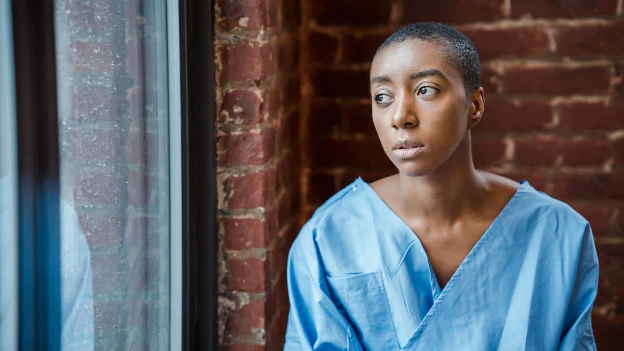 A person wearing a hospital robe looks out a window