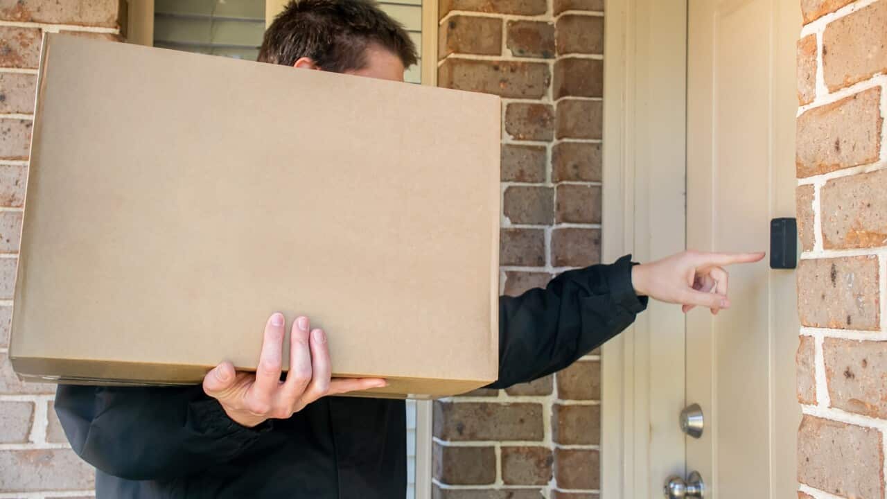 Courier delivery man holding a big cardboard box rings to the doorbell. Parcel delivery concept
