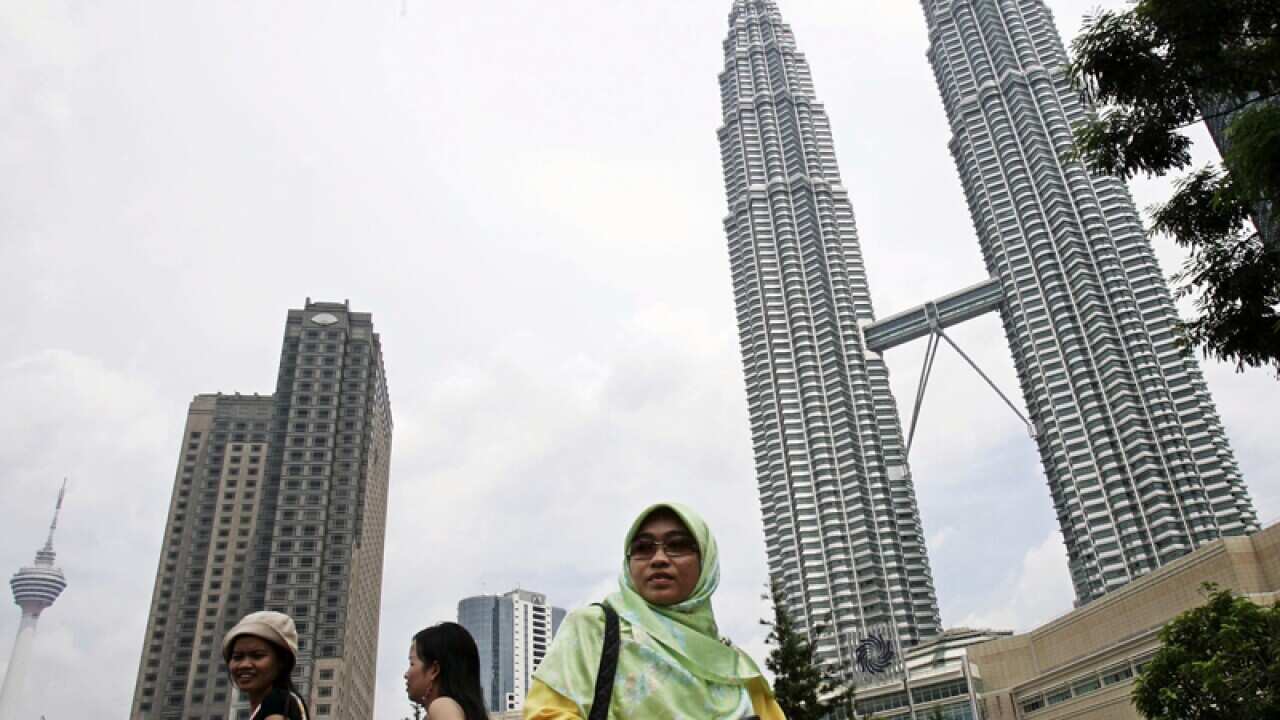 Malaysian women walk in front of Kuala Lumpur's Petronas Twin Towers